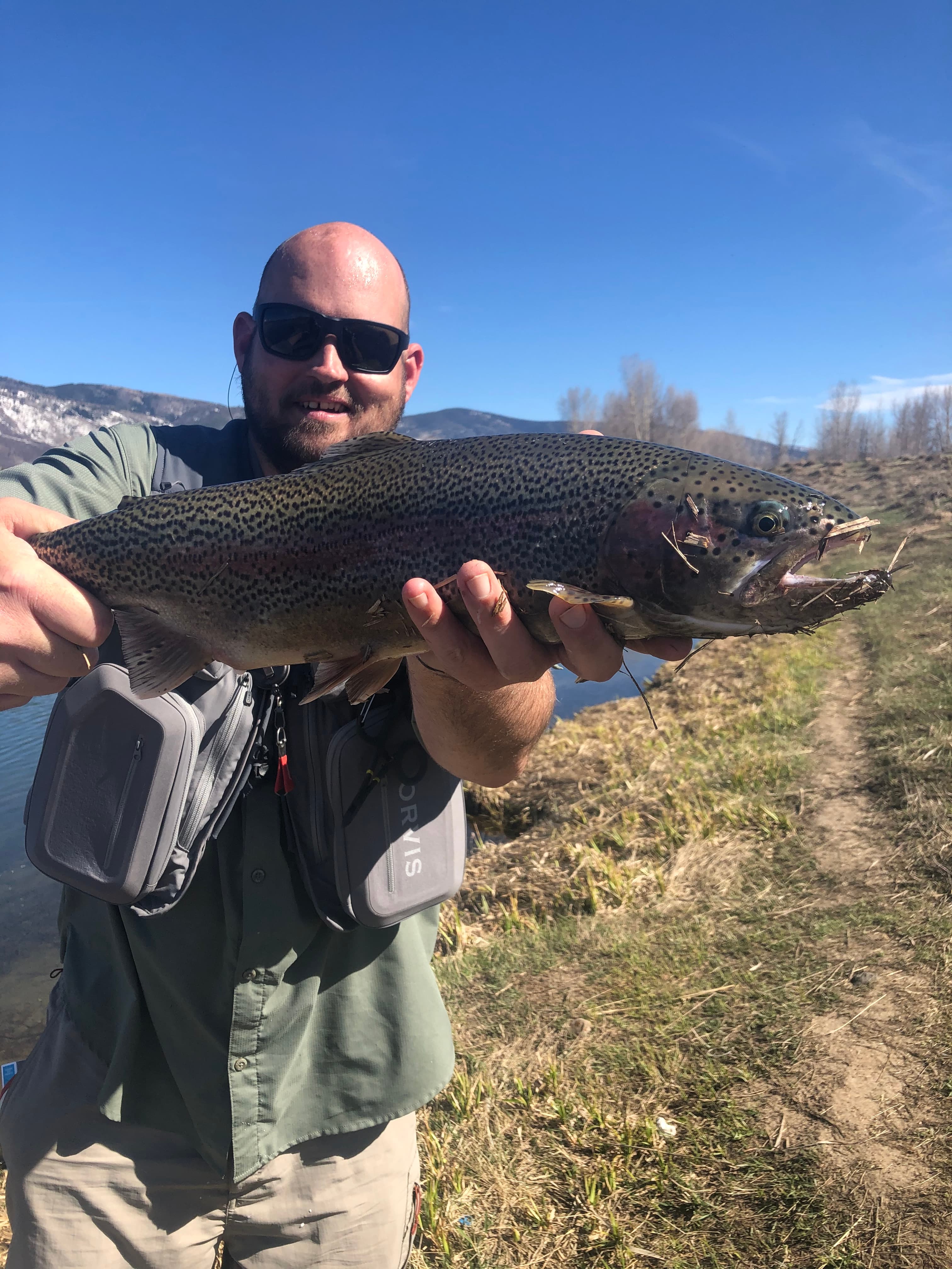 John fly fishing on a riverbank, holding a rainbow trout